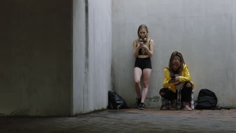 jóvenes multiétnicas que usan teléfonos inteligentes relajándose disfrutando de navegar por los mensajes de las redes sociales vistiendo moda de moda en un fondo urbano grungy