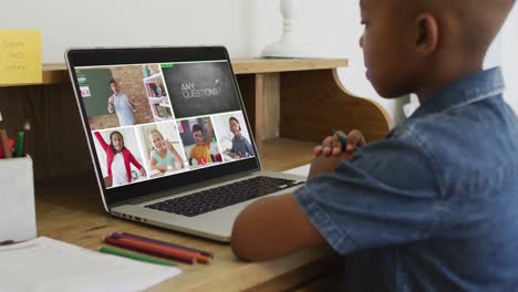 Schoolboy-using-laptop-for-online-lesson-at-home,-with-diverse-teacher-and-class-on-screen