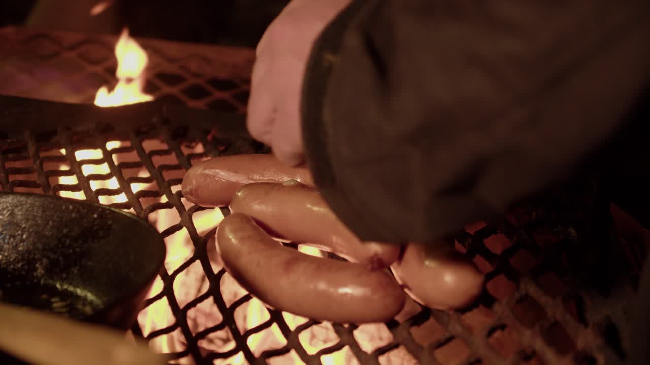 Sausages on hot metal grill over night camp fire are flipped by hand