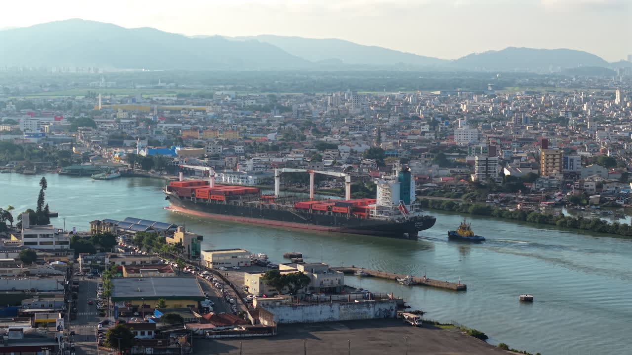 Aerial establishing fly Cargo Ship sailing Itajai Port in Brazil, Santa Catarina, city background, transportation hub