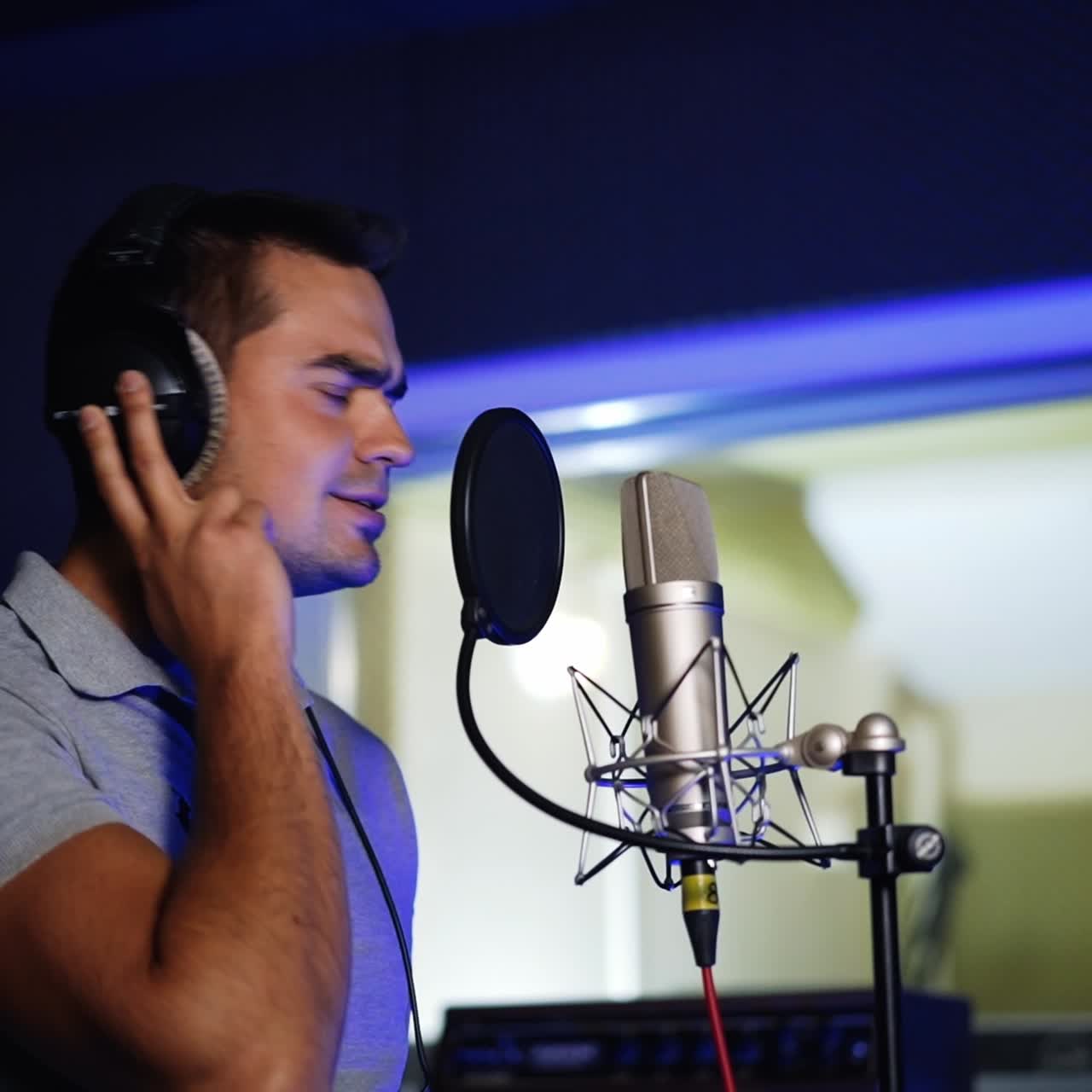Dark-haired handsome Caucasian man singing in the studio. Professional song recording in the specialized music company