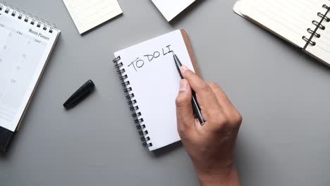 hand writing a to-do list in a notebook with a pen