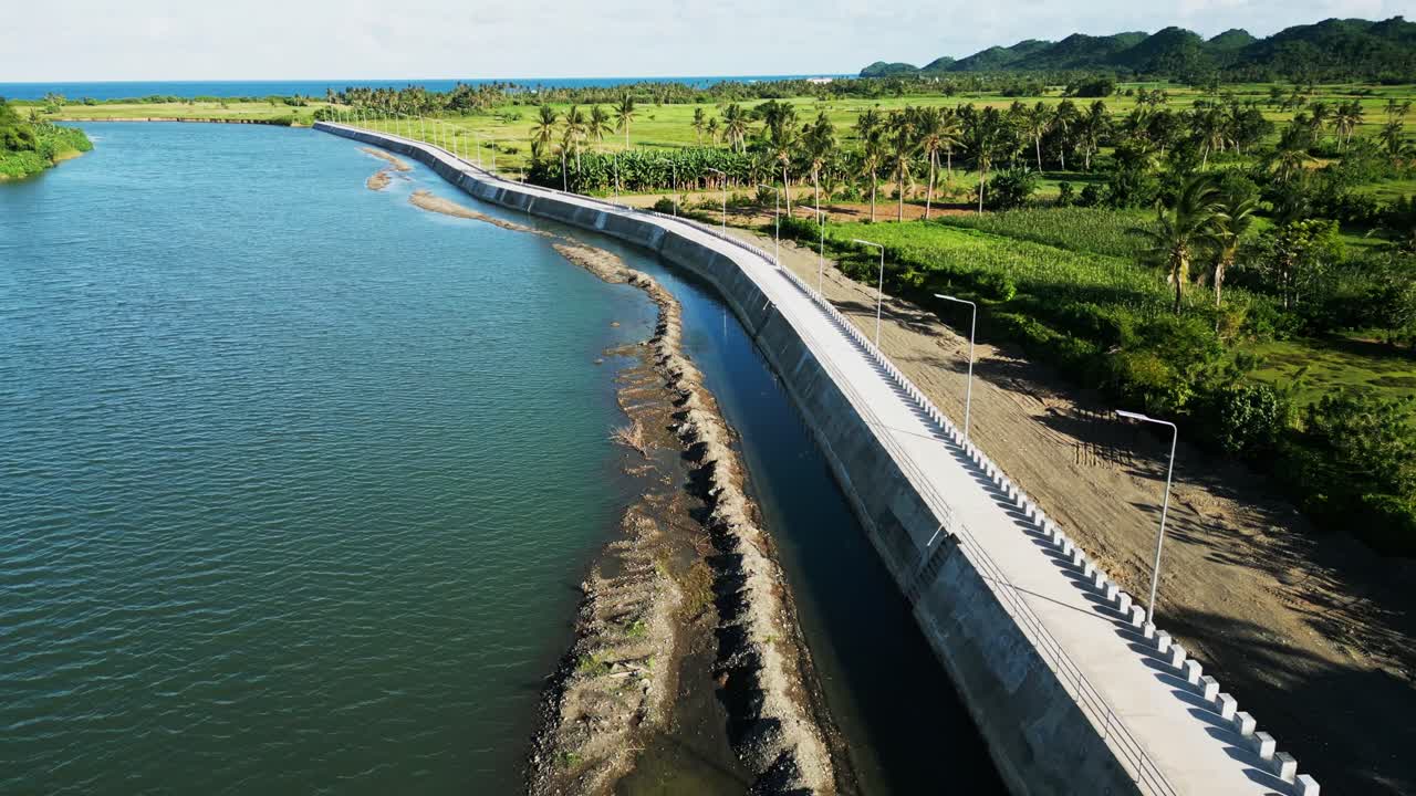 Aerial flyover shot of newly built dike and walkway along scenic Pajo river and tropical island greenery at Catanduanes, Philippines