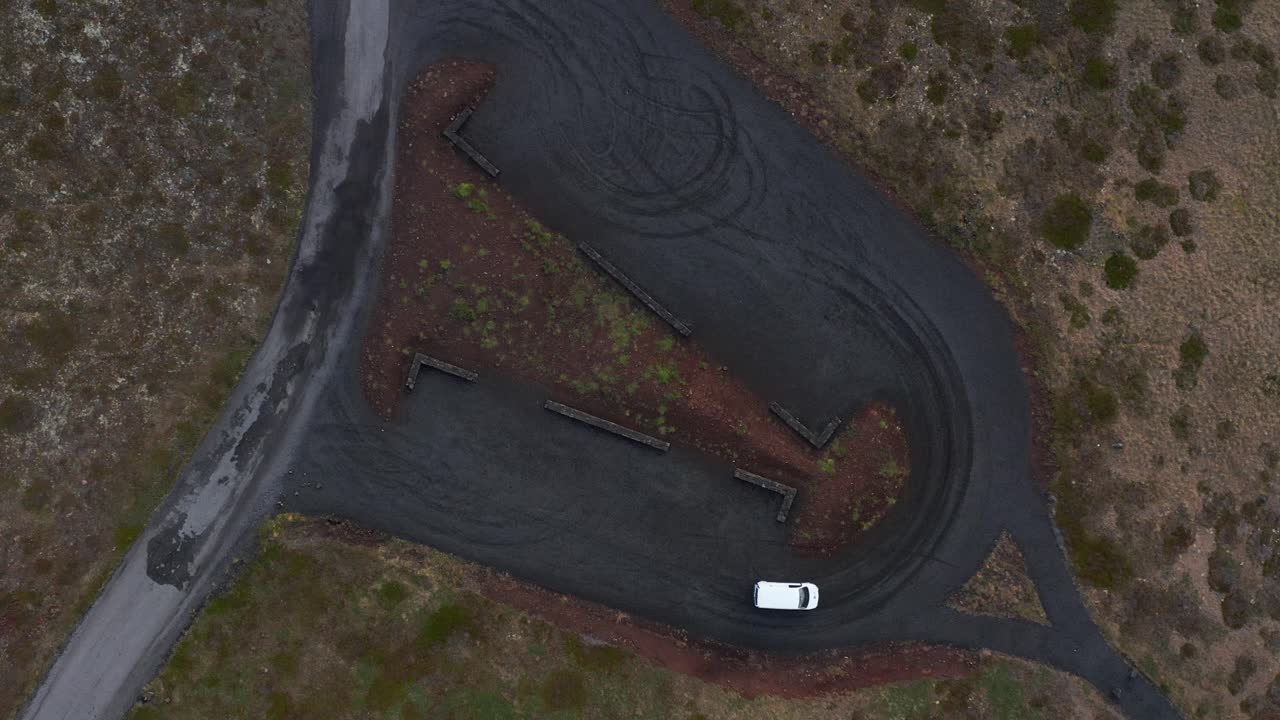coche girando en el estacionamiento de superficie de grava oscura en islandia, de arriba hacia abajo