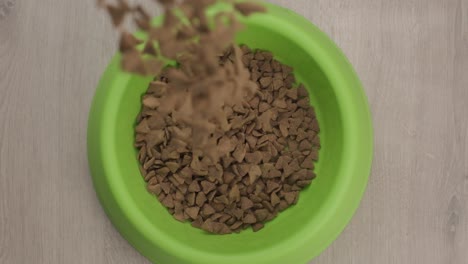 Top-down-view-Pet-food-pellets-poured-on-Green-bowl-over-wood-floor---Slow-motion