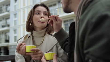 Pareja-Feliz-Disfrutando-De-Un-Helado-Al-Aire-Libre.-Hombre-Alimentando-A-Una-Mujer-En-La-Calle-Urbana.