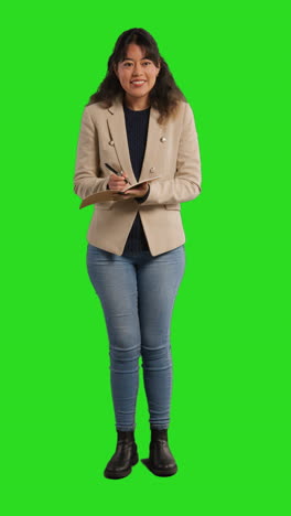 vertical video of female teacher in school classroom standing taking class register in front of green screen background