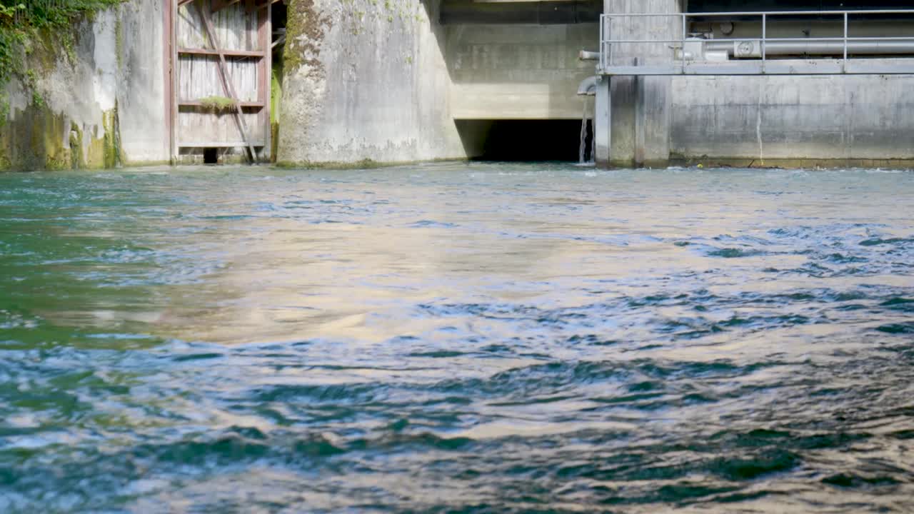 River water stream flowing in and out of a water-treatment plant dam, or a hydroelectric power plant in Switzerland, Europe. Real time, no people
