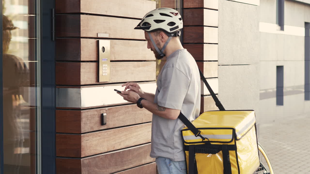 Food Delivery Guy Wearing Thermal Backpack Calls The Entry Phone Of A Building To Make A Delivery