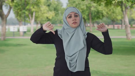 disappointed muslim woman showing thumbs down in park