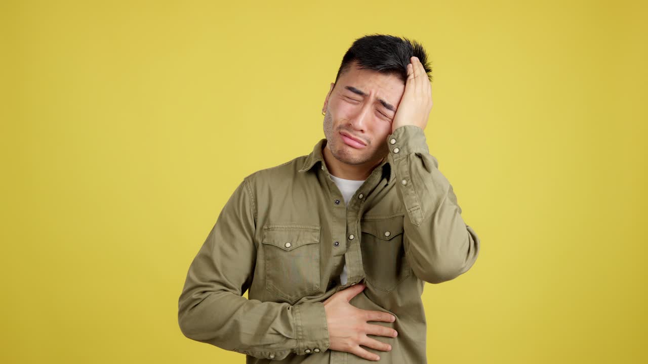 Man suffering from headache and stomach ache on a yellow background