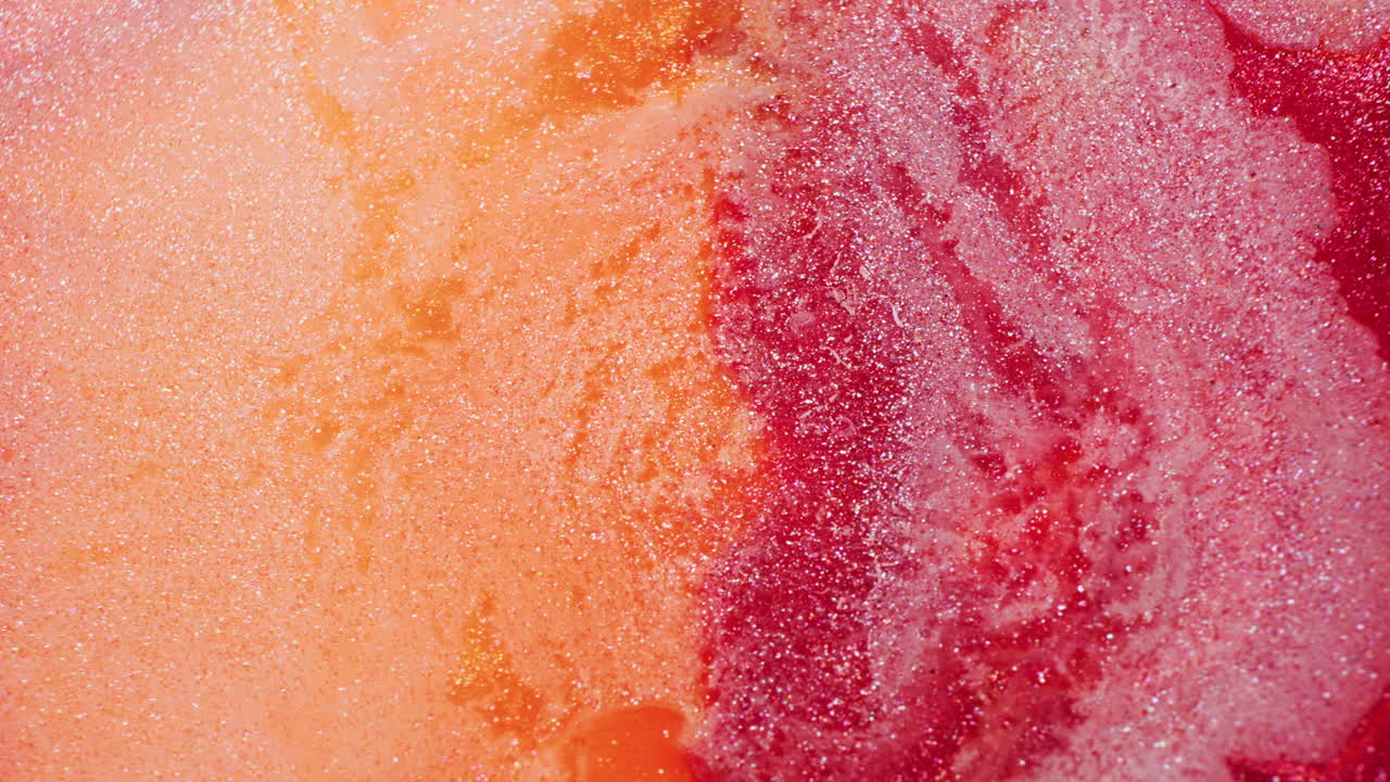 Macro shot of red and orange glitter ink dynamically pushed by a stream of air, creating vivid swirling motion and sparkles