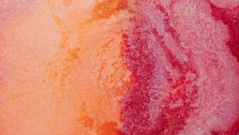 macro shot of red and orange glitter ink dynamically pushed by a stream of air, creating vivid swirling motion and sparkles