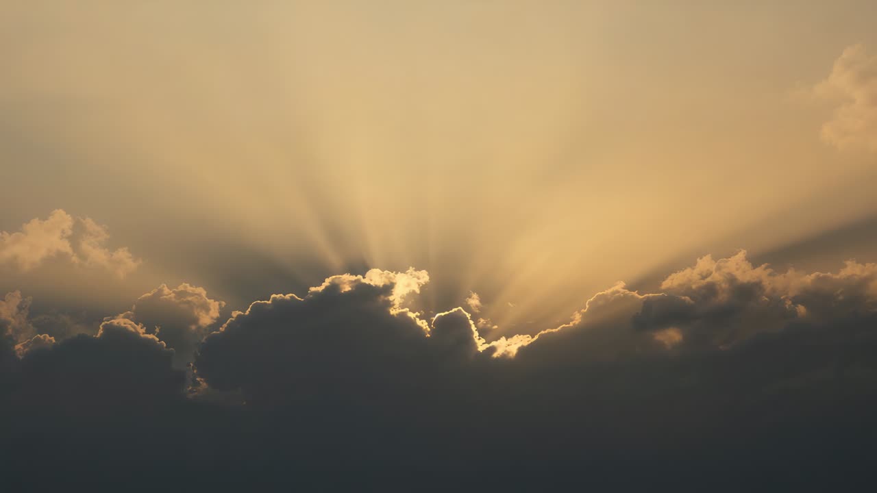 Parting cumulus cloud bank revealing sun peeking, casting warm golden sunbeams at sunrise