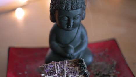 small buddha statue with burning smoking lavender sage sitting on red asian plate in slow motion