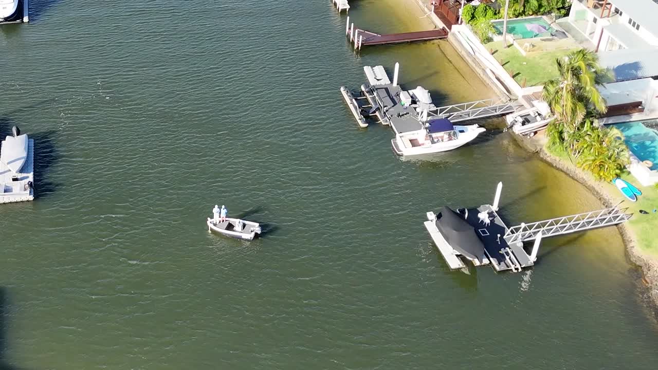 Aerial view of boats moored at a residential canal with clear skies and calm waters.