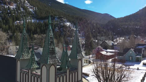 Gothic-church-in-the-foreground-in-breckenridge-town,-colorado-filled-with-snow---drone-shot