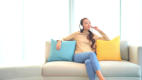 a pretty young woman sitting on a couch between colorful decorative pillows while listening to music through her headphones