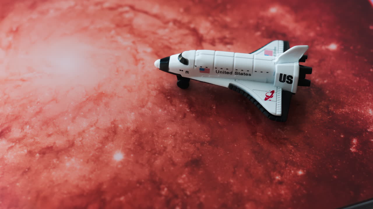Close up of a miniature toy space shuttle placed on a reddish galaxy background