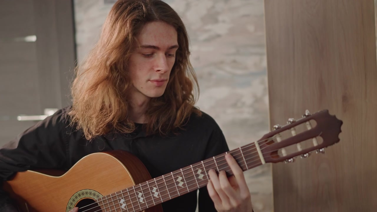 Giovane chitarrista insegna brani classici in uno studio accogliente, guidando lo studente nella tecnica fingerstyle, primo piano sulle mani, luce naturale calda, espressione attenta, rosetta ornata di chitarra acustica.
