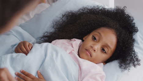 mother caring for sick daughter ill in bed taking temperature with thermometer