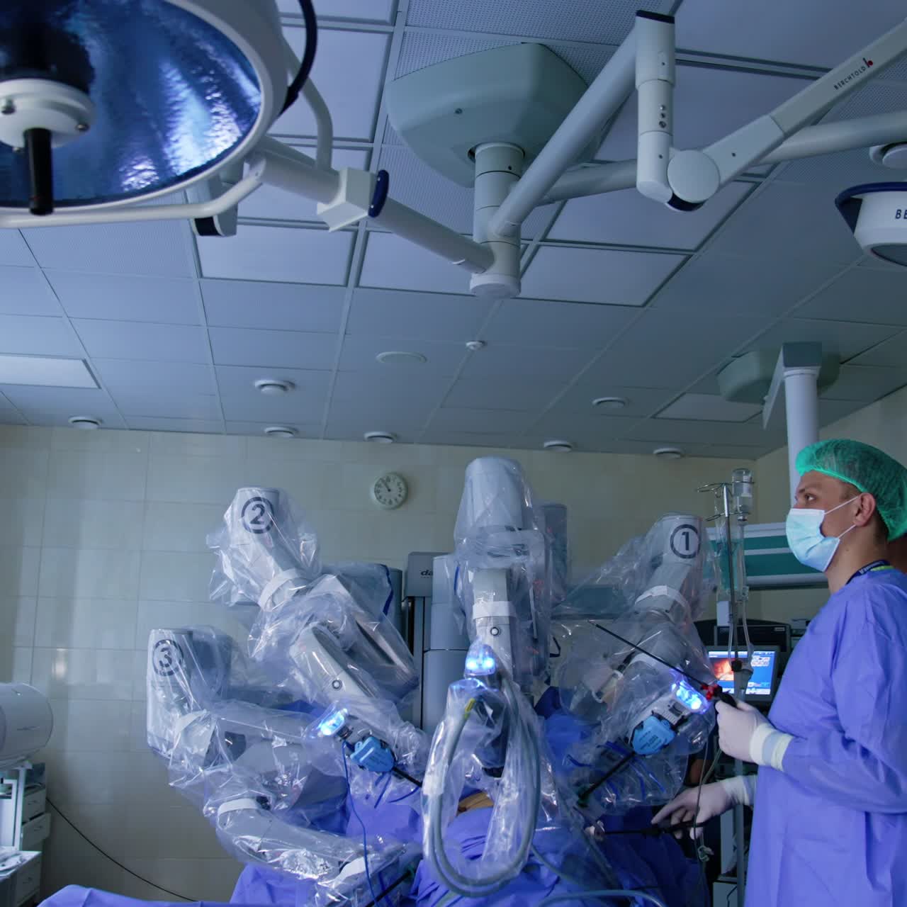 Modern surgical room with Da Vinci robot performing surgery. Male doctor watches the procedure on the monitor