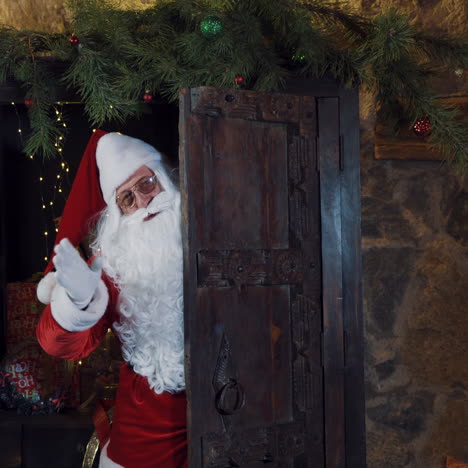 santa is waving his hand while standing at the door. christmas decorations and santa claus in red costume showing bye gesture by hand.