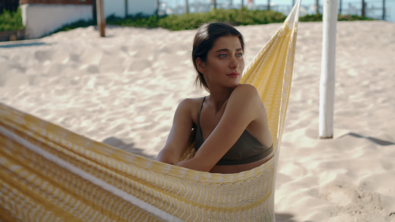 Serene woman enjoying hammock on sandy beach. Smiling girl relaxing ocean shore