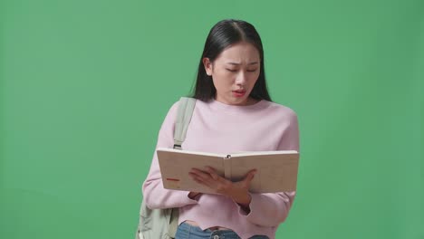 심각한 아시아 여성 학생이 녹색 스크린 스튜디오에서 책을 읽고