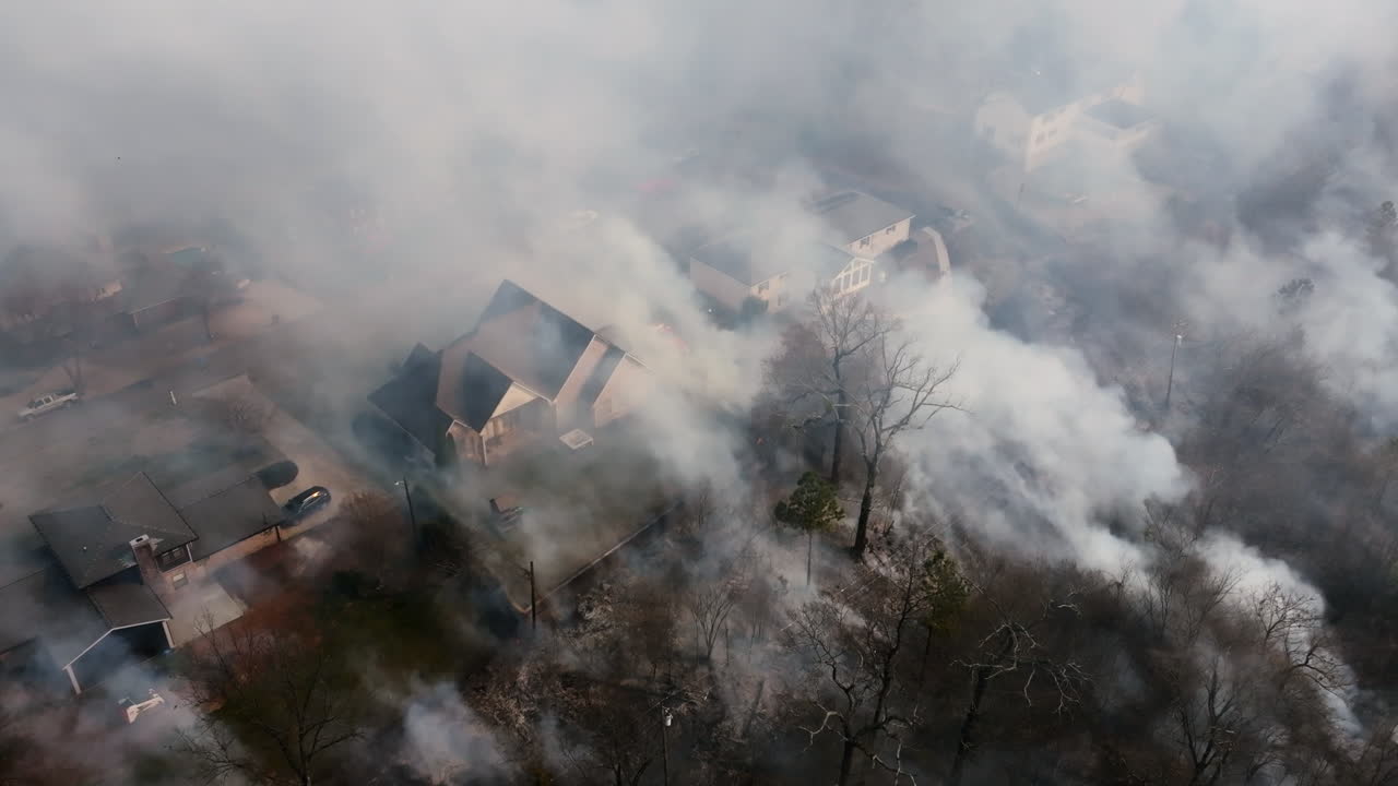 Close up aerial footage of houses that are covered in smoke from a wildfire that is very close to the neighborhood.