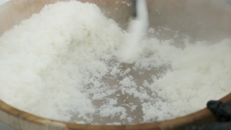 cook stirs hot rice in a wooden bowl