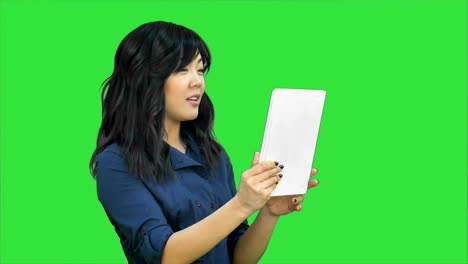 una mujer de negocios asiática hablando usando una tableta en una pantalla verde, llave cromática
