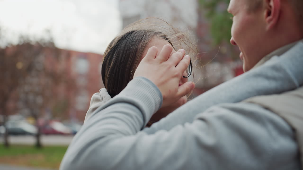 Young couple staring into each other eyes as man gently adjusts woman hair blown by wind, sharing quiet romantic moment outdoors with soft expressions of love and connection on their faces