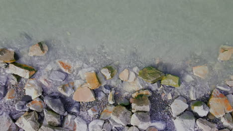 aerial topdown view rising shot of ocean lapping onto rocks, slow upward drone