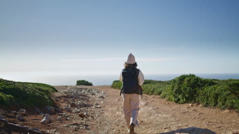 Girl-backpacking-ocean-view-on-sunny-day-vertical.-Tourist-exploring-walk-trail