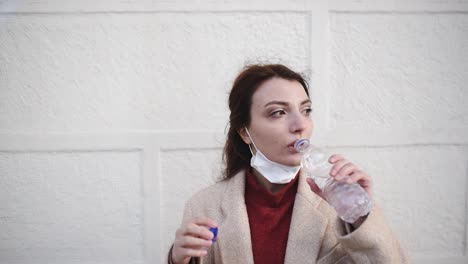 hermosa chica con máscara médica protectora y ropa de moda bebe agua con botella
