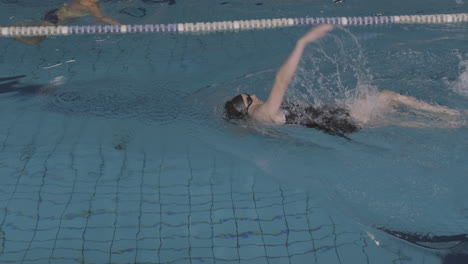 lateral tracking shot of a young female swimmer swimming backstroke in an indoor pool