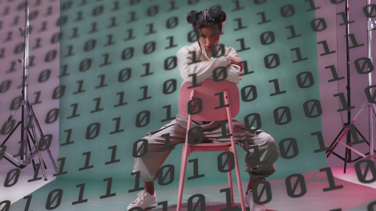 Model unzipping jacket showing dark top, shifting on pink chair while binary code shifting, studio