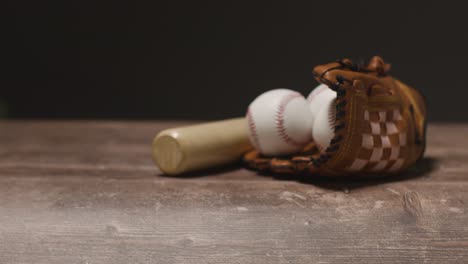 studio baseball shot with catchers mitt and person picking up wooden bat and ball from wooden background 1