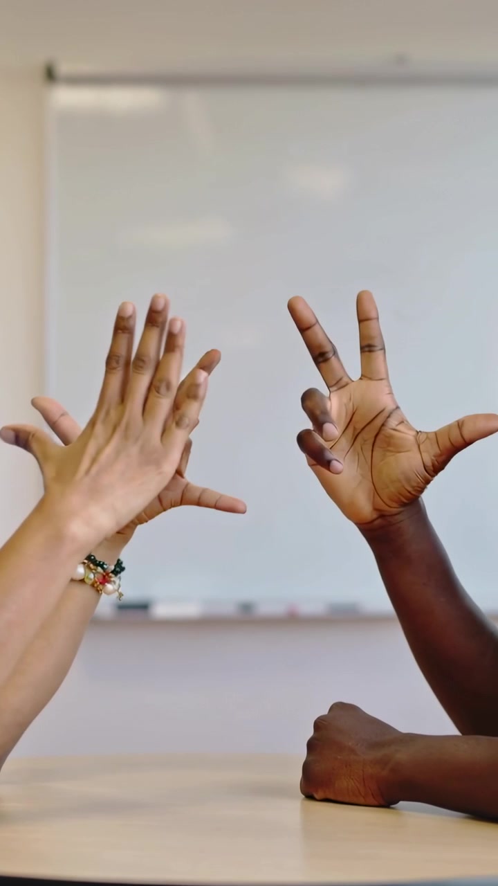 Vertical video: Lifting hands, two adults mirroring gestures signaling at round table by whiteboard