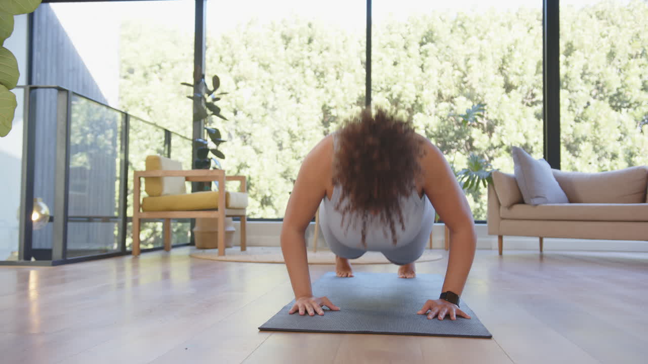 Exercising on yoga mat, plus size woman doing push-ups in modern living room