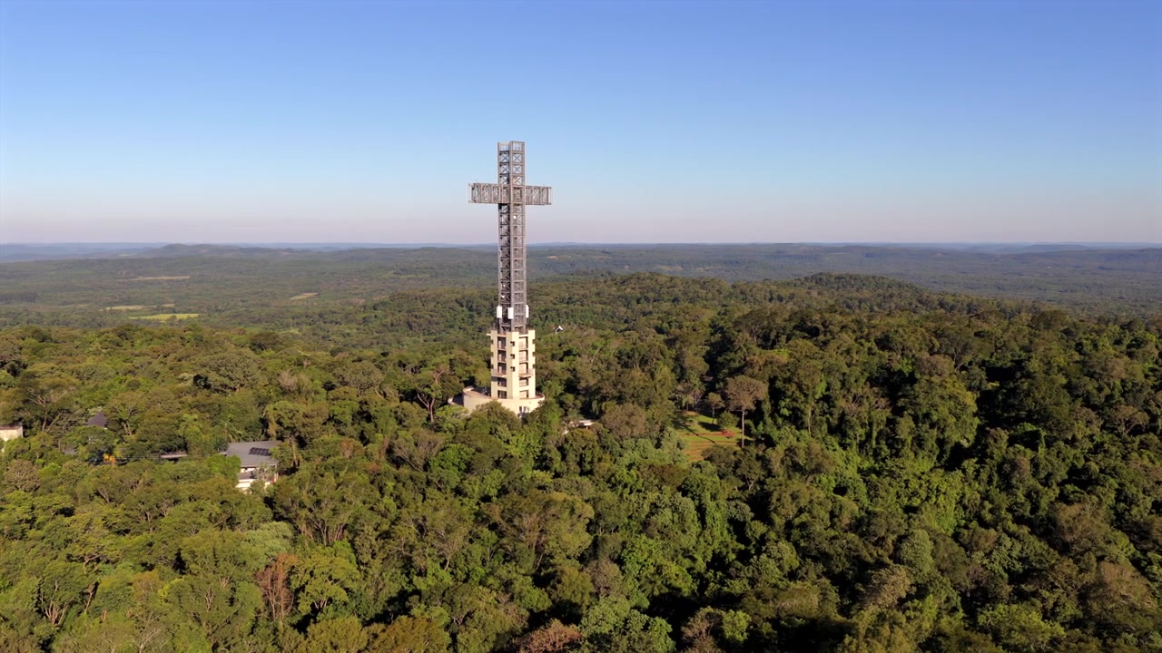 Uma cruz imponente ergue-se em meio a uma floresta densa no Parque Temático de la Cruz, Santa Ana, Argentina. Ideal para conteúdo de viagem ou documentários culturais.