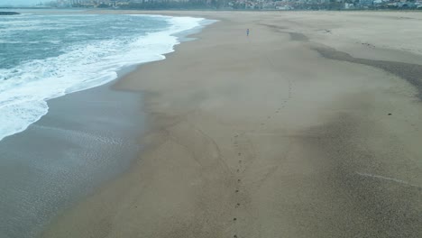 Stunning-aerial-view-drone-jogger-running-beach-ocean-sea-waves-breaking-on-coastal-landscape,-wonderful-fitness-health-training-concept-in-nature,-single-man-on-beach,-city-background-porto,-portugal