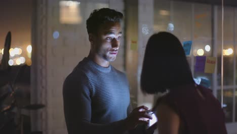 Diverse-male-and-female-colleague-using-tablet,-brainstorming-on-glass-wall-at-night-in-office