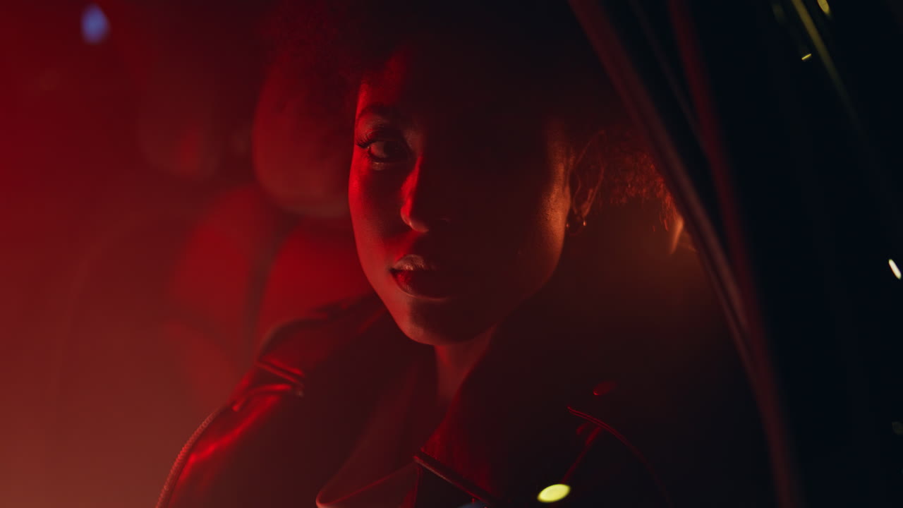 Serious woman sitting car illuminated red light at night closeup. lady