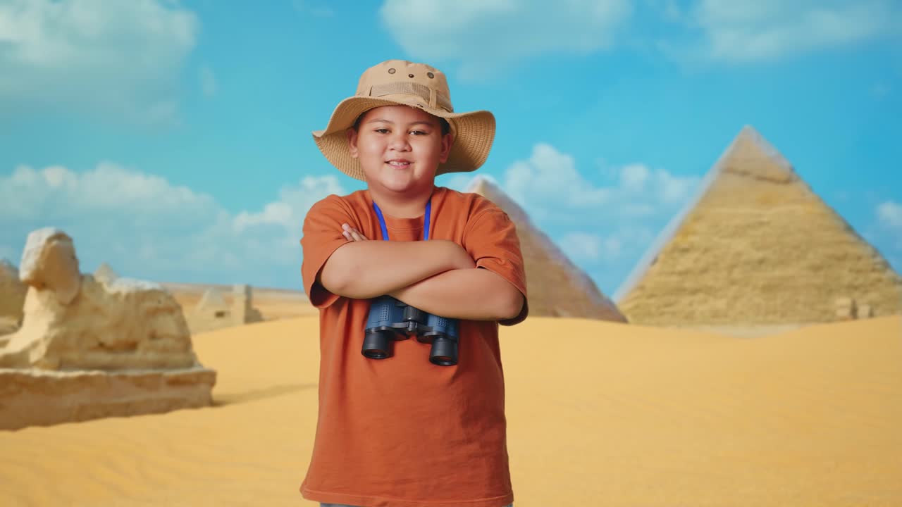 Asian Boy With A Hat And Binoculars Crossing Arms And Smiling To Camera While Traveling In Giza Pyramid. Boy Researcher Examines Something, Travel Tourism Adventure Concept