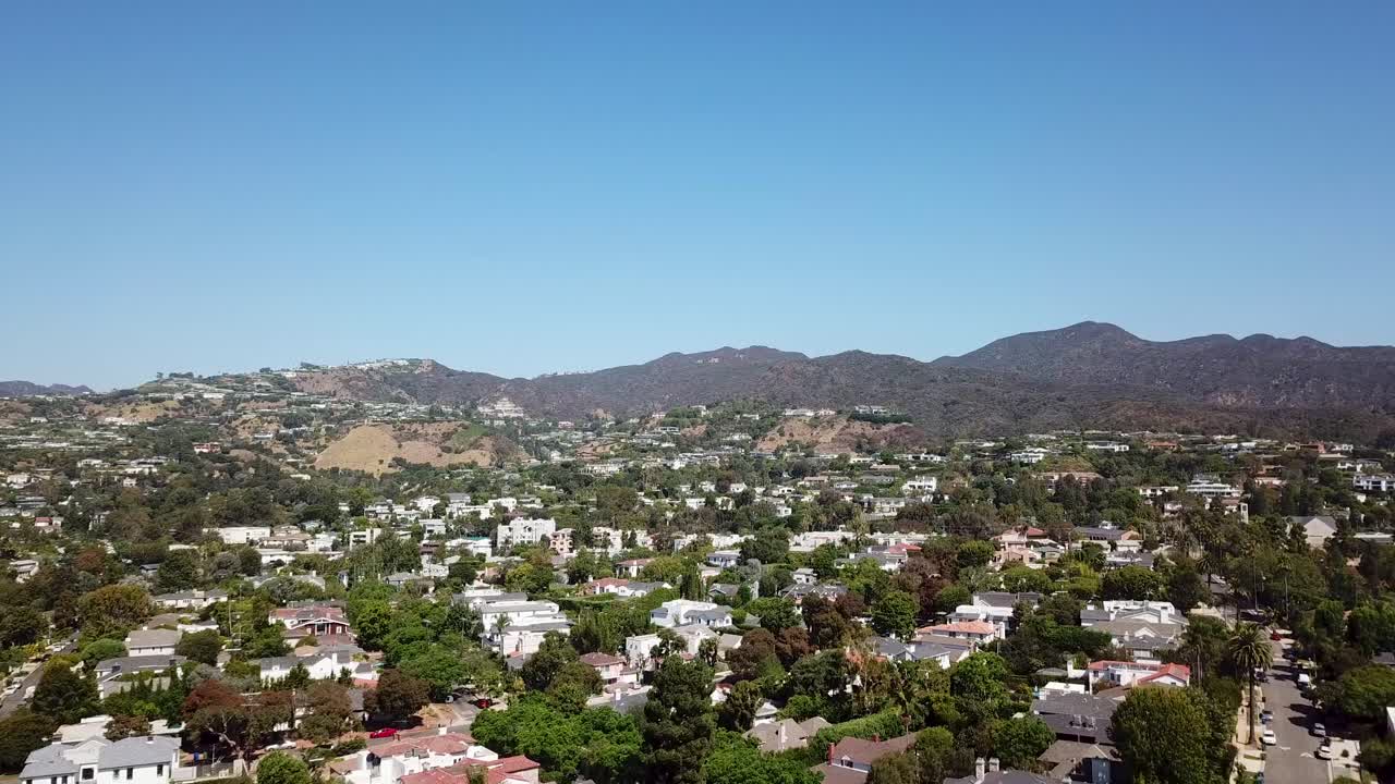 Aerial flyover Pacific Palicades district of Los Angeles during sunny day. Blue sky with mountains in background. Luxury villas and mansion during beautiful autumn day. Wide shot