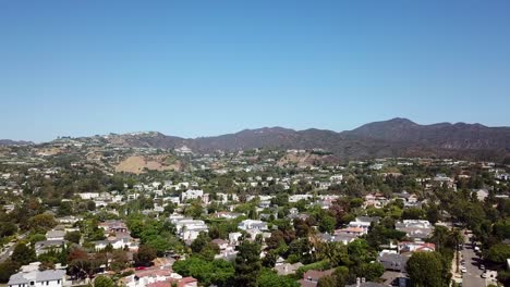 aerial flyover pacific palicades district of los angeles during sunny day. blue sky with mountains in background. luxury villas and mansion during beautiful autumn day. wide shot