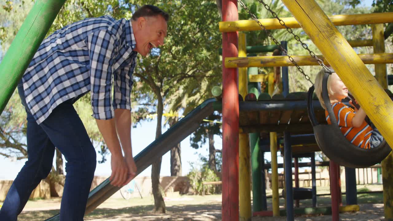 padre empujando a su hijo en el columpio en el patio de recreo 4k