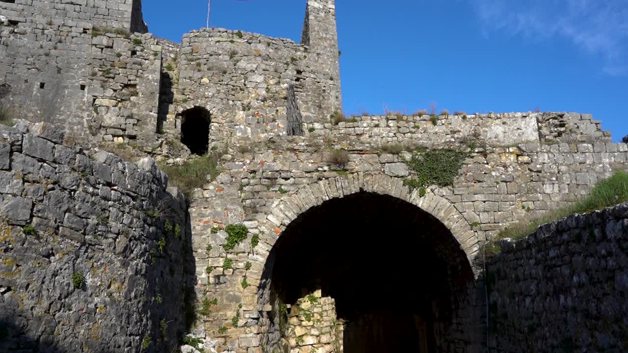 большие ворота входа в замок с арочными каменными стенами и красным флагом в шкодере, албания